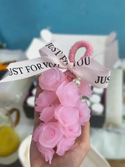 Chùm xà phòng hình hoa hồng màu hồng cầm trên tay, nơ in chữ “Dành riêng cho bạn”